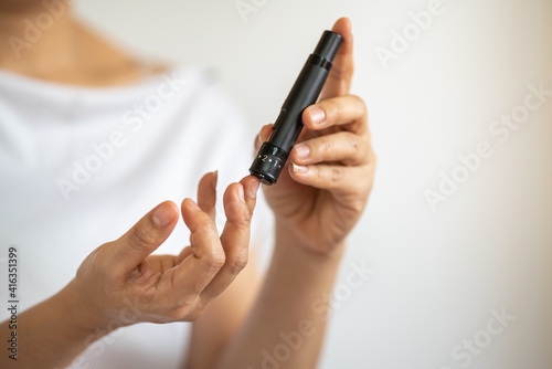 Close up of woman hands using lancet on finger to check blood sugar level by Glucose meter. Use as Medicine  diabetes  glycemia  health care and people concept.