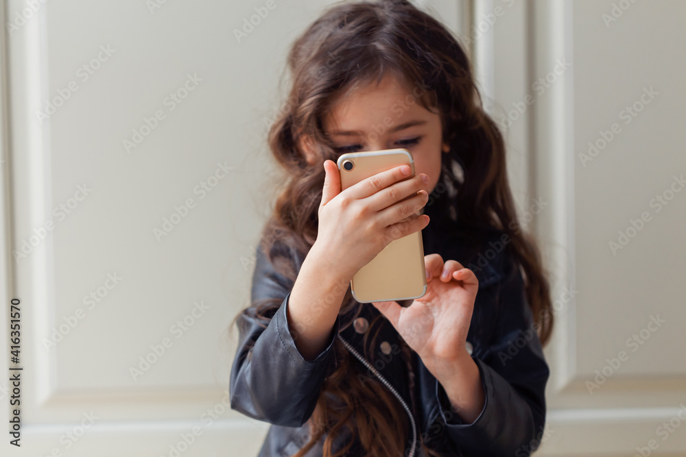 A little girl sits on the floor in her room and using a smartphone A little girl sits on the floor in her room and using a smartphone
