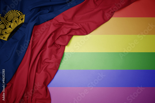 waving national flag of liechtenstein on a gay rainbow flag background.