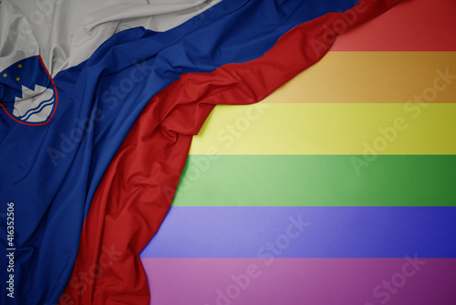 waving national flag of slovenia on a gay rainbow flag background.