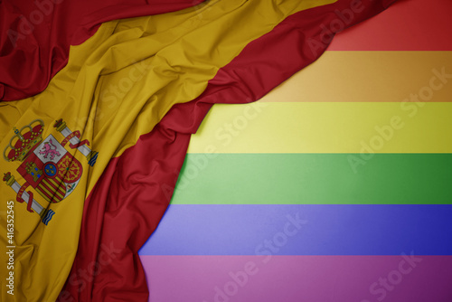 waving national flag of spain on a gay rainbow flag background.