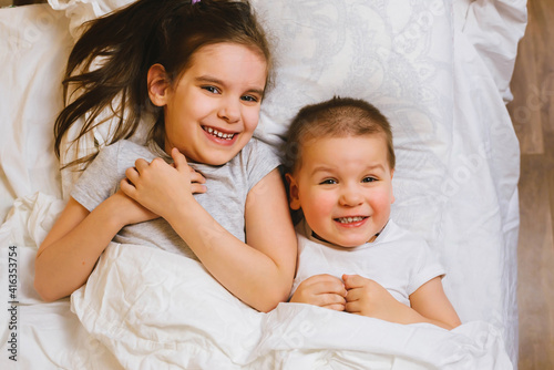Happy Family Brother and Sister Relaxing Together, Laughing and Playing in Bed in the Early Morning. Healthy Sleep, Wake up, Laugh Concept.