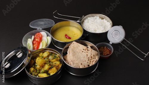 Typical Stainless steel Lunch Box or Tiffin with Maharashtrian food menu Chapati OR Roti, Plain Dal Tadka, White Rice Potato sabji with salad and pickle photo