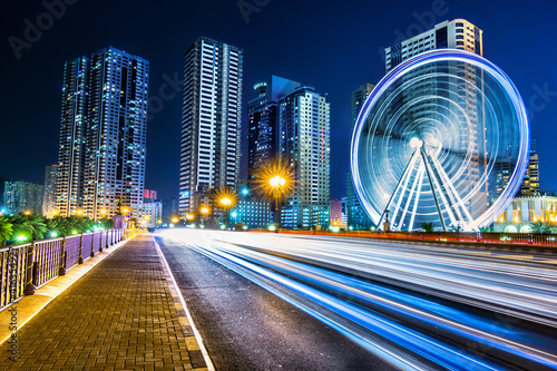 City at night with spinning Ferris wheel and running cars and tail lights lines 