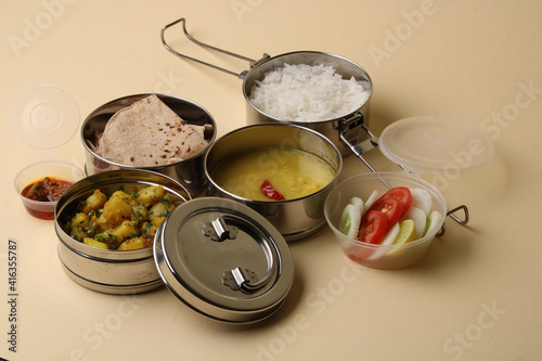 Typical Stainless steel Lunch Box or Tiffin with Maharashtrian food menu Chapati OR Roti, Plain Dal Tadka, White Rice Potato sabji with salad and pickle photo