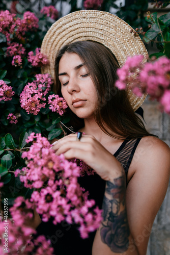 Brunette girl with long hair in hat surrounded with pink flowers  © innadril