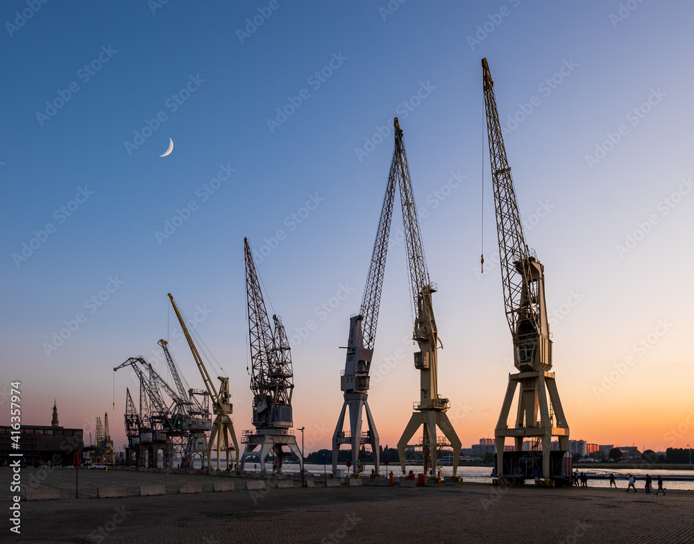 Obraz premium Old harbor crane silhouettes under a crescent moon. Antwerp, Belgium.