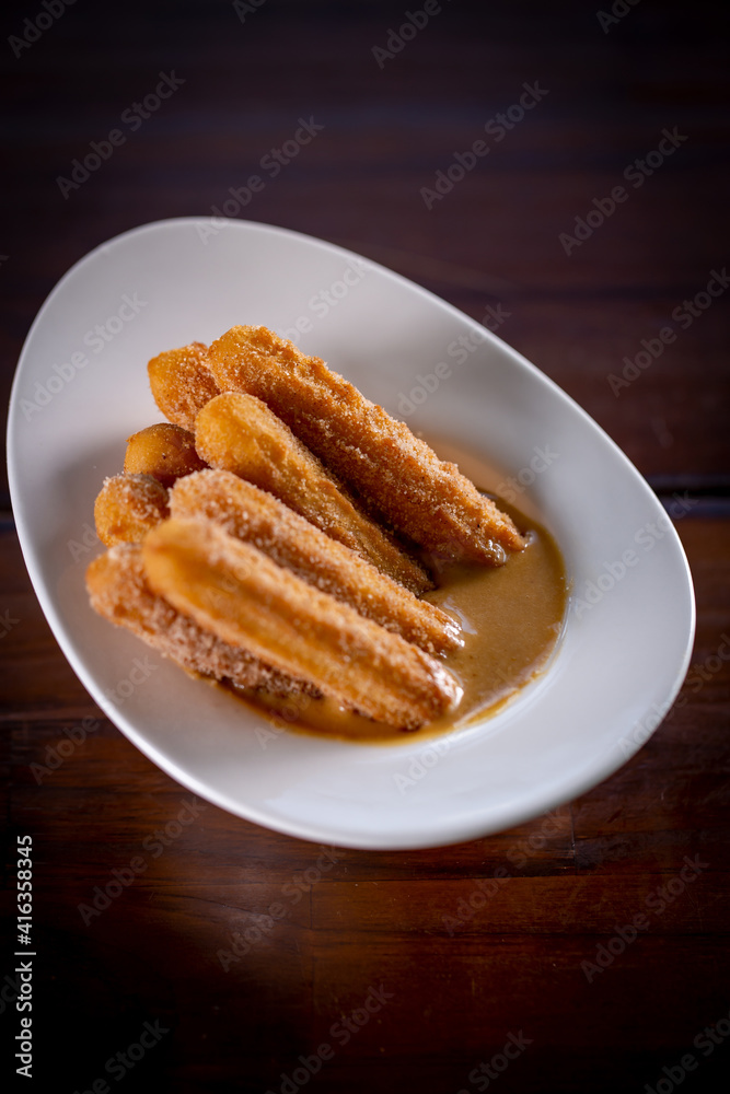 Churros sticks with caramel in a wooden background Churros sticks with caramel in a wooden background