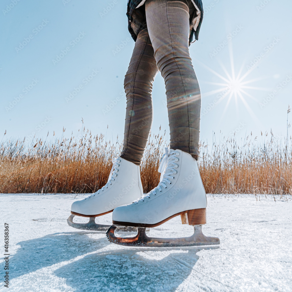 Young woman ice skating outdoors on a pond on a freezing winter day. Detail  of skate shoes. Photos | Adobe Stock
