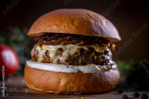 Craft beef burger with cheese, caramelized onion and sauce on wooden background