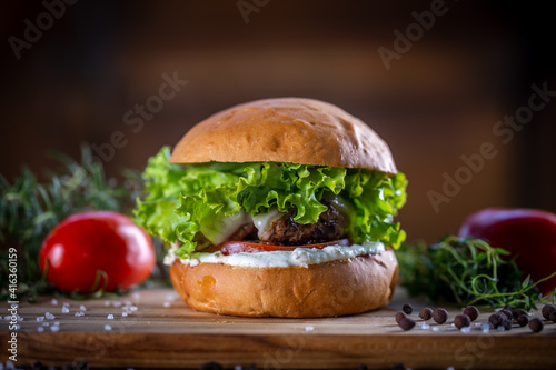 Craft beef burger with cheese, lettuce, tomato and sauce on wooden background