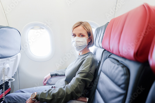 Young woman wearing face mask is traveling on airplane. New normal travel covid-19 pandemic concept.
