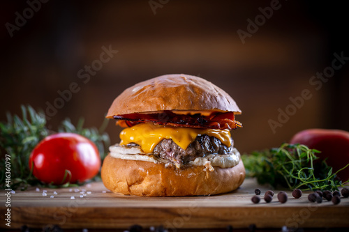 Craft beef burger with cheddar, bacon and sauce on wooden background