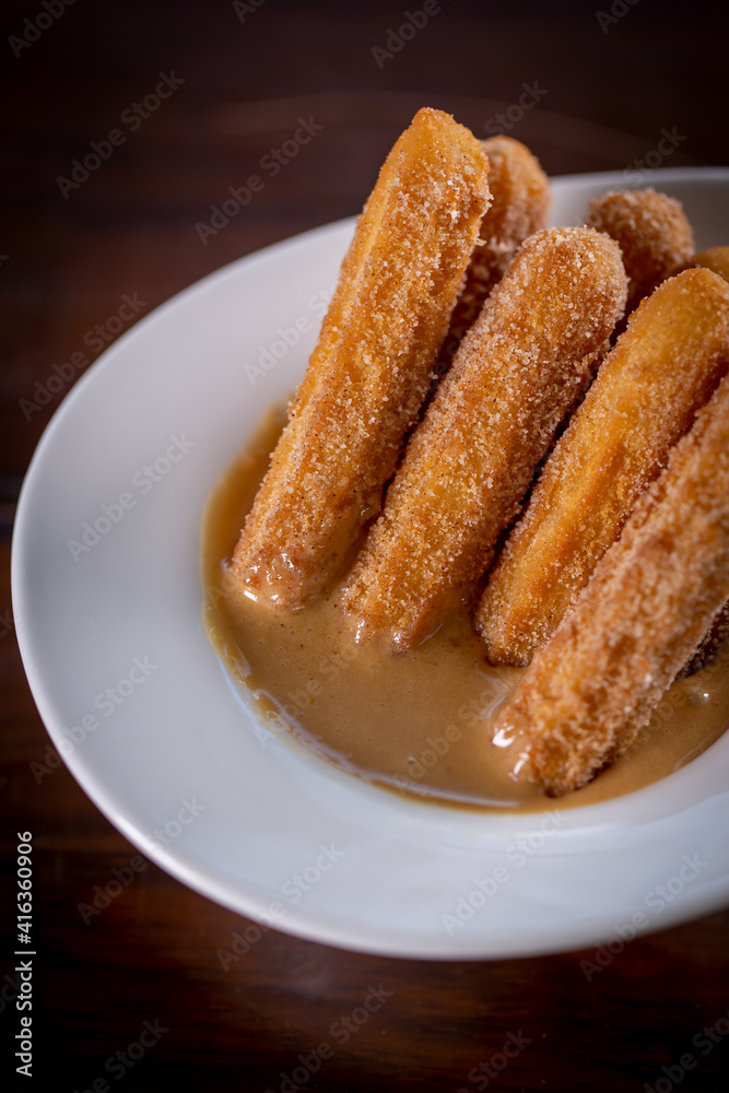 Churros sticks with caramel in a wooden background Churros sticks with caramel in a wooden background