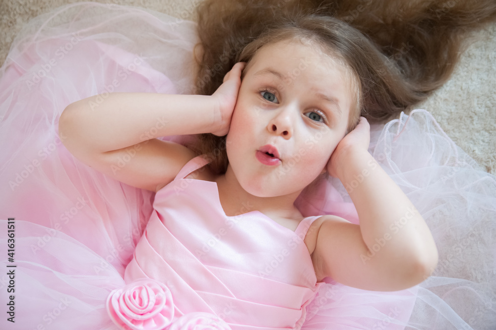 A cute little girl in a lush pink dress lies on her back and makes cute faces A cute little girl in a lush pink dress lies on her back and makes cute faces