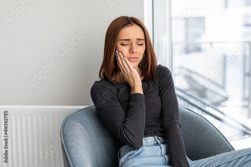 Portrait of young woman with toothache sitting in chair at home