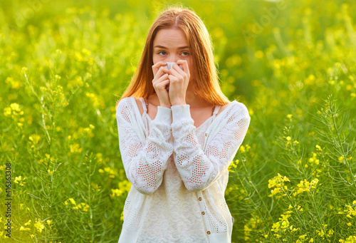 Allergic to pollen and flowering season, a redhead girl sneezing on a field