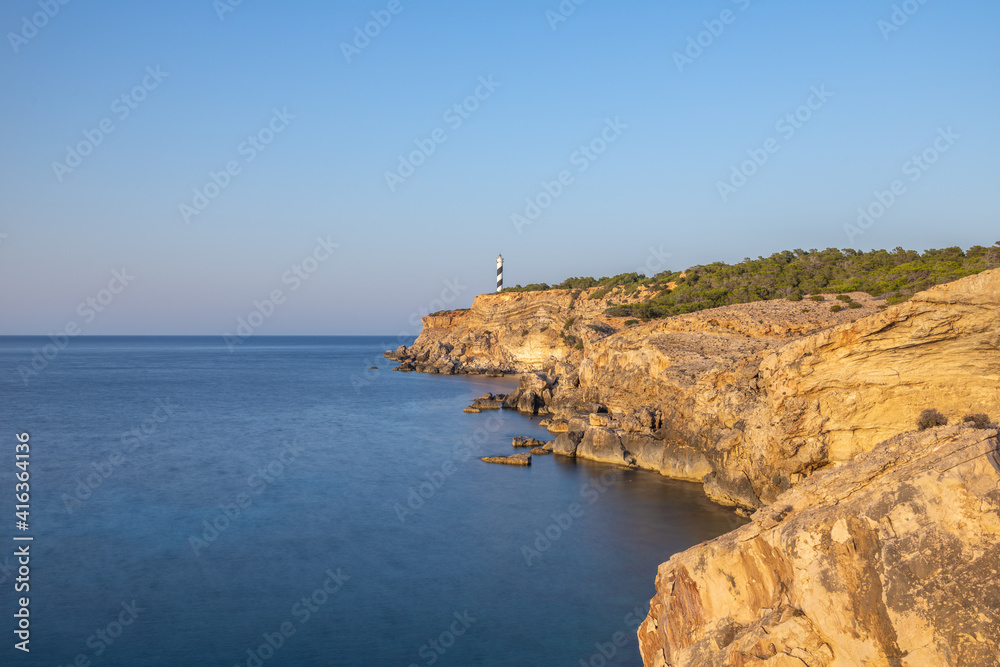 Faro en el borde de un acantilado con un mar suavizado por una larga exposición y un cielo de verano azul eléctrico 