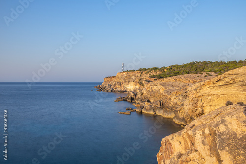 Faro en el borde de un acantilado con un mar suavizado por una larga exposición y un cielo de verano azul eléctrico 