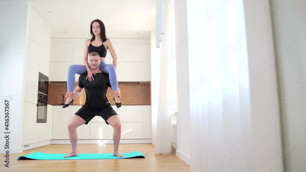Muscular Bodybuilder Athletic Man and Beautiful Fitness Woman in Workout Clothes are Doing Squat Exercises in Apartment. family team together. young couple squatting at home. two fit people together Muscular Bodybuilder Athletic Man and Beautiful Fitness Woman in Workout Clothes are Doing Squat Exercises in Apartment. family team together. young couple squatting at home. two fit people together