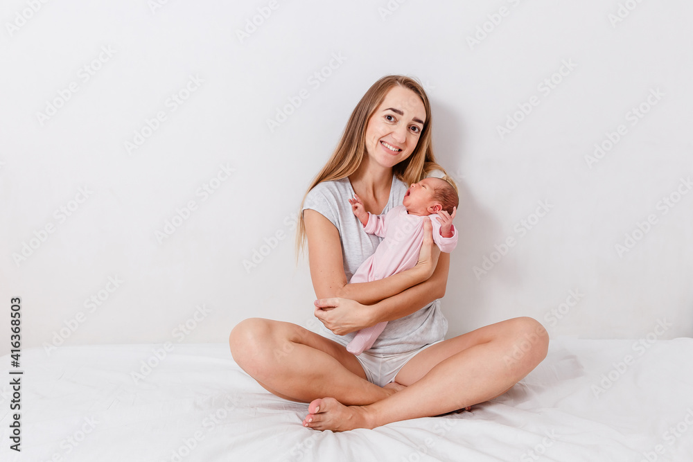 Happy mother holds newborn baby girl sitting on bed Happy mother holds newborn baby girl sitting on bed