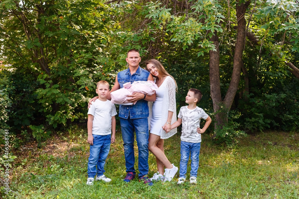 Obraz premium Happy parents and two children of preschoolers and newborn baby washed into the camera on a natural green background in the summer