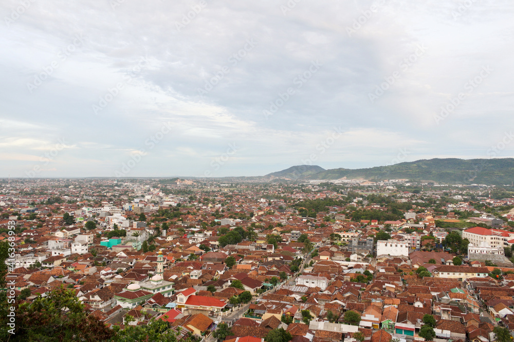Aerial view of dense city and population of Bandar Lampung cityscape with horizon and coastline in background. Strange cloud formation. Cloudy blue sky. 