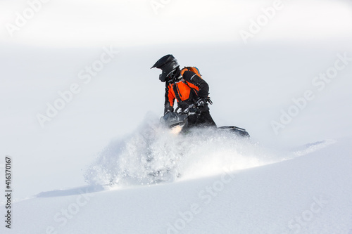 A man in protective equipment on a snowmobile rides along the snowy slopes.