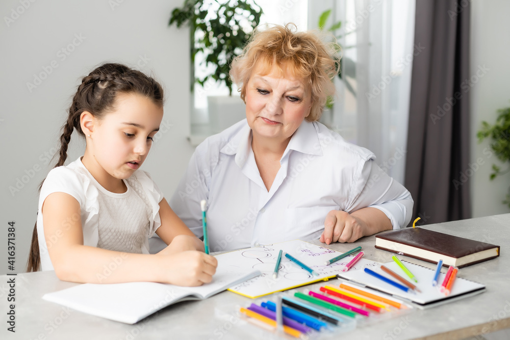 Happy grandchild with grandmother having fun, drawing colored pencils, sitting together at home, laughing preschool girl with smiling grandma painting picture, playing with granddaughter Happy grandchild with grandmother having fun, drawing colored pencils, sitting together at home, laughing preschool girl with smiling grandma painting picture, playing with granddaughter