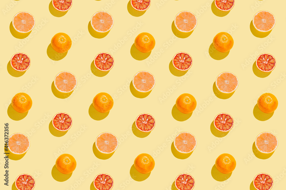 Creative pattern made with sliced grapefruit and blood orange on yellow background. Summer fruit concept. Sunlit flat lay. Top view Creative pattern made with sliced grapefruit and blood orange on yellow background. Summer fruit concept. Sunlit flat lay. Top view