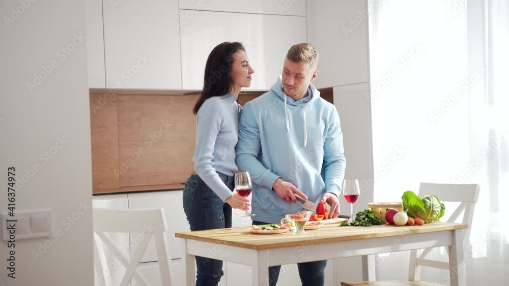 Loving young married couple husband and wife cooking healthy food together in the modern kitchen at home. Spend time together to prepare a vegetable salad and drink wine. Happy and cheerful family Loving young married couple husband and wife cooking healthy food together in the modern kitchen at home. Spend time together to prepare a vegetable salad and drink wine. Happy and cheerful family