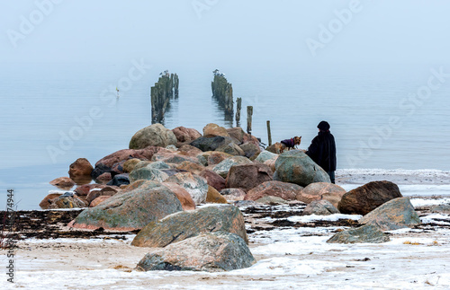 Foggy morning at old broken pier with walking woman and small dog