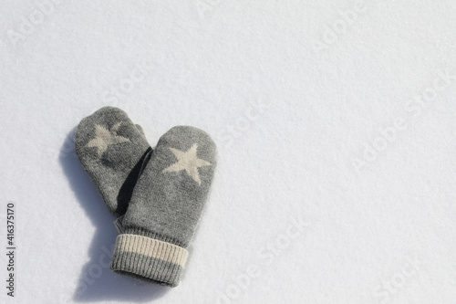 Beautiful knitted gray mittens with a star on white snow.
