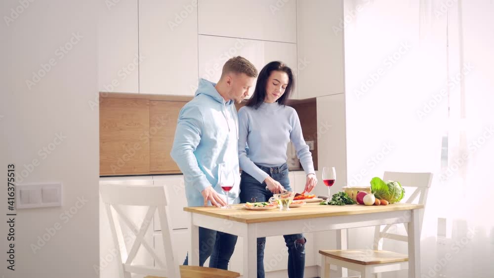 Loving young married couple husband and wife cooking healthy food together in the modern kitchen at home. Spend time together to prepare a vegetable salad and drink wine. Happy and cheerful family Loving young married couple husband and wife cooking healthy food together in the modern kitchen at home. Spend time together to prepare a vegetable salad and drink wine. Happy and cheerful family
