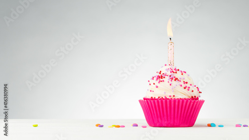 Birthday cupcake. Tasty cupcakes with white cream icing and colored sprinkles. Burning candle in a cake. Sweet delicious dessert on white wooden table. White Background with Copy space.