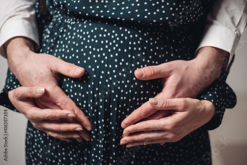 A pregnant woman holds her husband's hands on her belly