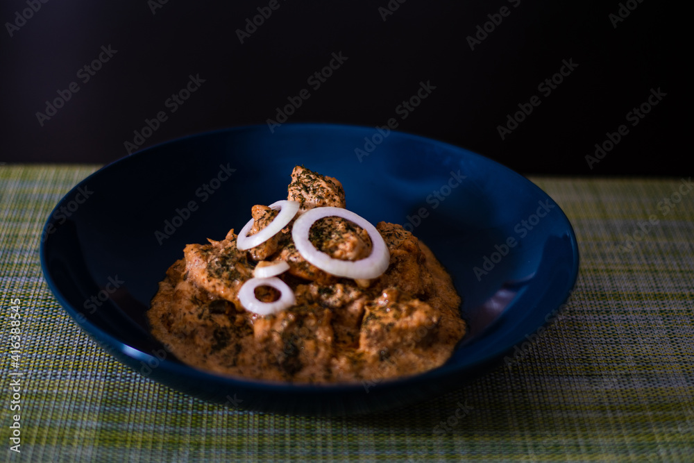 Delicious chicken butter masala curry in a blue bowl garnished with green chopped leaves with a wooden background Delicious chicken butter masala curry in a blue bowl garnished with green chopped leaves with a wooden background