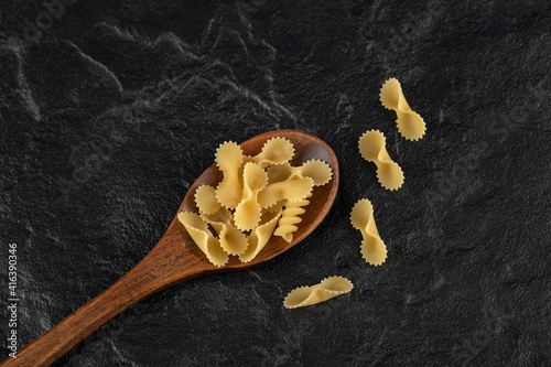 A wooden spoon full of raw farfalle tonde macaroni