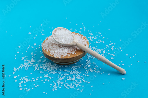  Crystals of Dead Sea salt in a wooden spoon on a wooden stand on a blue background close-up.