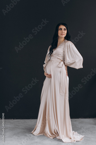 Studio portrait of beautiful pregnant woman is wearing nice long dress and holding her belly