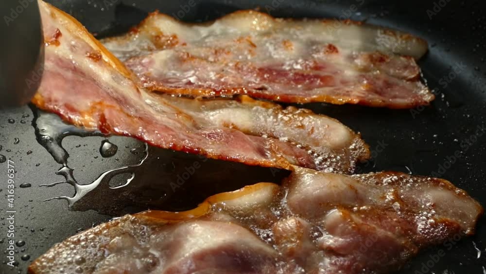 Fry the bacon in a pan. A slice of pork bacon is prepared in its own fat. Layer of meat and lard. Close up in the kitchen.