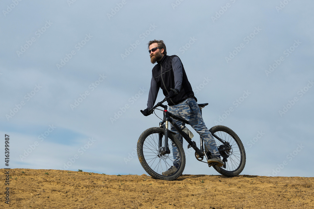 Sports brutal bearded guy on a modern mountain bike. Beautiful view from the mountain. Panoramic view for banner.