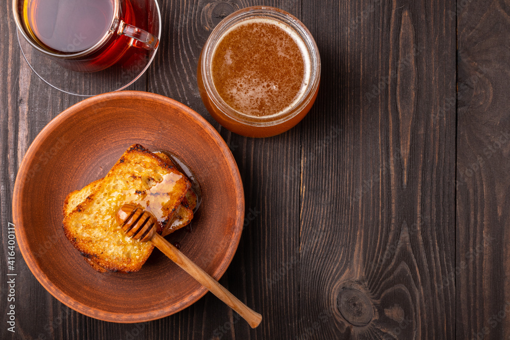 slices of bread dripped with honey in a ceramic plate with a jar of honey an a cup of black tea on a dark wooden background top view slices of bread dripped with honey in a ceramic plate with a jar of honey an a cup of black tea on a dark wooden background top view