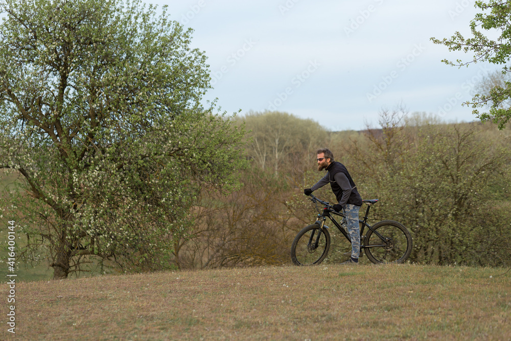 Sports brutal bearded guy on a modern mountain bike. Cyclist on the green hills in the spring. Sports brutal bearded guy on a modern mountain bike. Cyclist on the green hills in the spring.