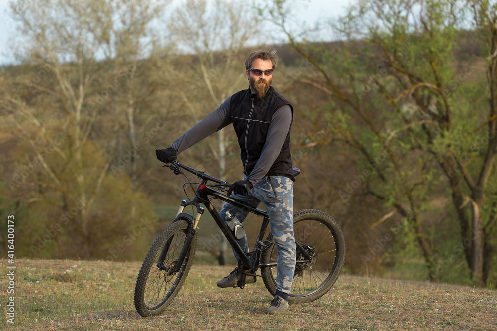 Sports brutal bearded guy on a modern mountain bike. Cyclist on the green hills in the spring. Sports brutal bearded guy on a modern mountain bike. Cyclist on the green hills in the spring.