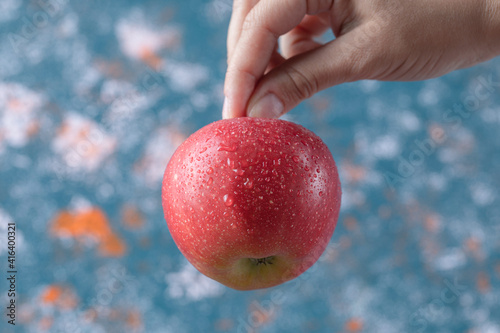 Holding a red apple from stem on blue background