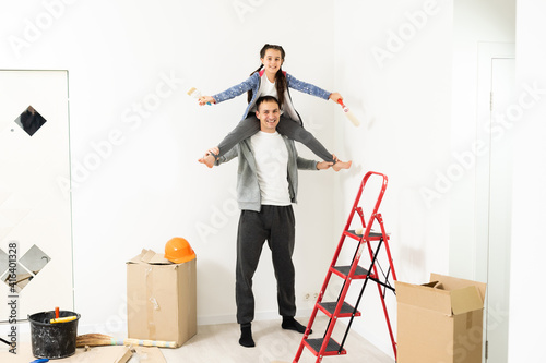 Happy young family renovating their home, paint a wall with a paint roller, the mother is standing on the ladder and smiling