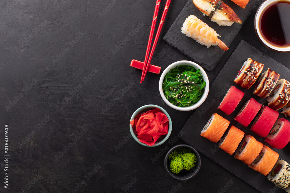 Various kinds of sushi placed on black slate board, seaweed salad, soy sauce in a bowl and ginger on the side. Asian food composition on black background, top view, copy space Various kinds of sushi placed on black slate board, seaweed salad, soy sauce in a bowl and ginger on the side. Asian food composition on black background, top view, copy space