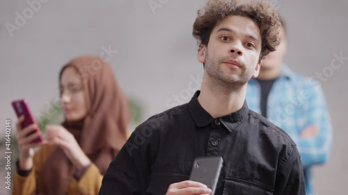 Portrait of nervous millennial Middle Eastern man waiting in queue indoors checking time on smartphone. Anxious hurrying young guy in cafeteria or at ATM. City lifestyle. photo