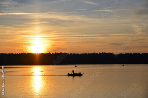 Orange sunset over the lake with silhouette of fisherman boat. Selective focus.